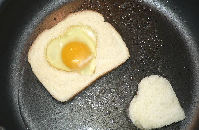 Egg inside a heart shaped hole in a bread in a skillet